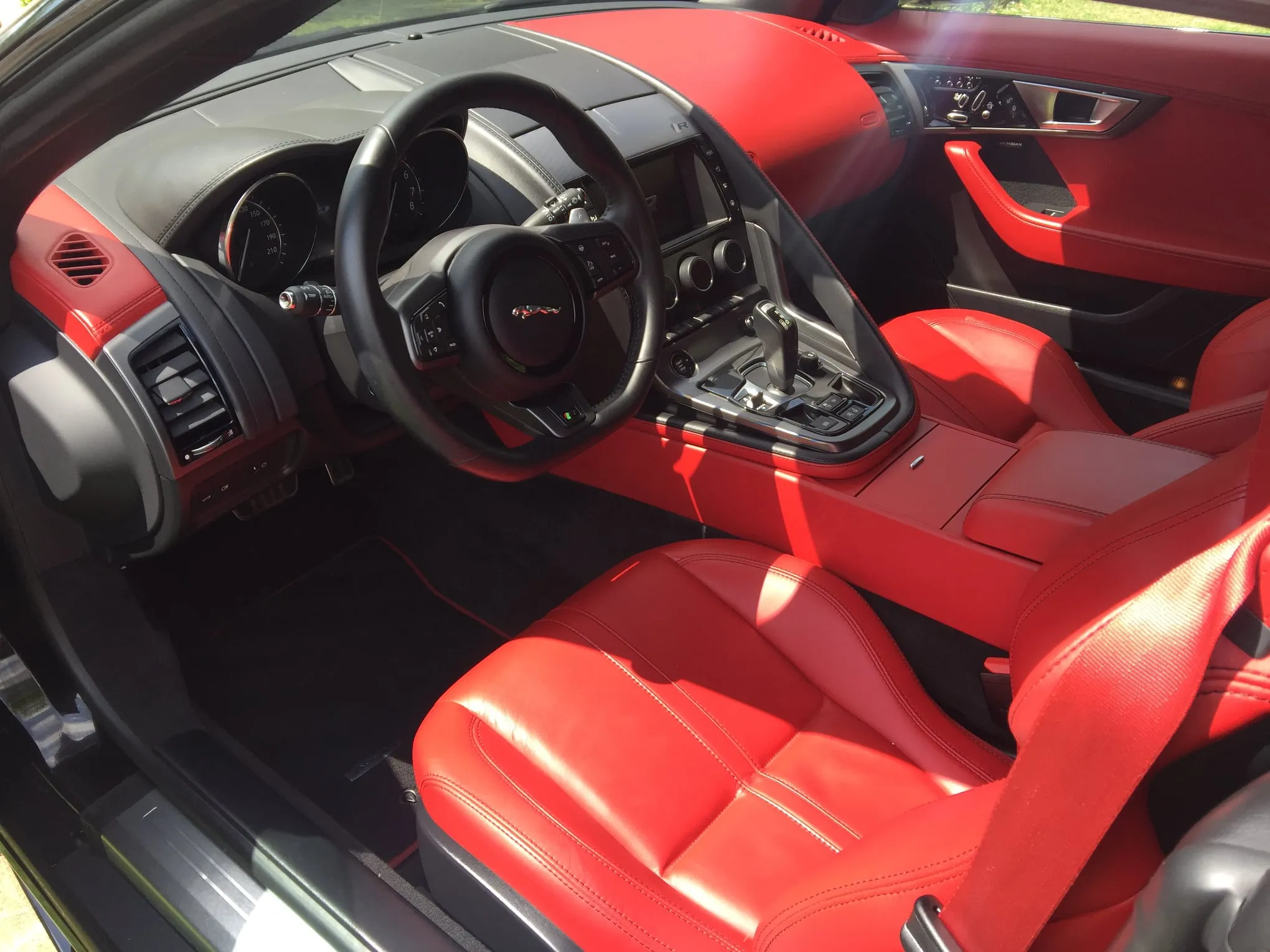 Interior of a luxury car featuring red leather seats, a black steering wheel with a Jaguar logo, and a center console with gear shift and controls.